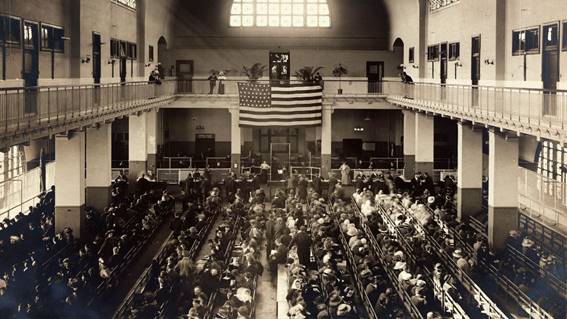 Immigrants are seated on long benches in the Registry Room at Ellis Island in New York Harbor. 