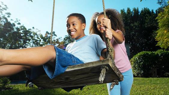 A girl pushes a wooden swing that a boy is sitting on.