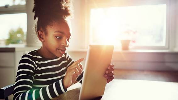 A girl works on a tablet computer. Bright sunlight streams through the window.